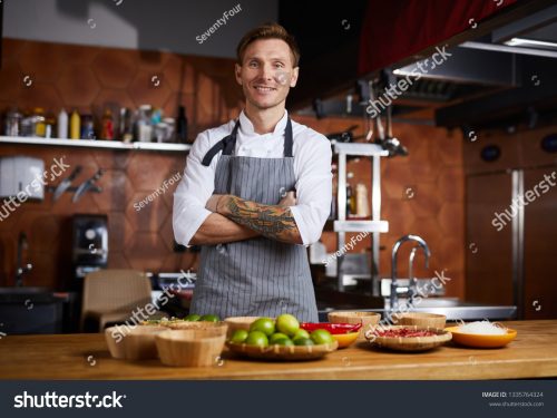 stock-photo-waist-up-portrit-of-handsome-chef-posing-standing-at-table-with-spices-copy-space-1335764324